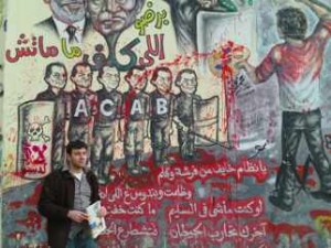 War Resister staff person Ali Issa in front of a mural stating, in part: "Oh regime which is scared of a paintbrush and a pen. You oppress us â€¦ If you were doing what you should be doing, you wouldnâ€™t be afraid." (photo by Tamar Sharabi)